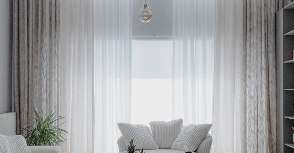 Sheer linen curtains hung high and wide on a window in a light and minimal small living room